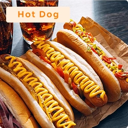 Trio de cachorros-quentes com mostarda e acompanhamentos variados, servidos em embalagem de papel com copos de refrigerante ao fundo.